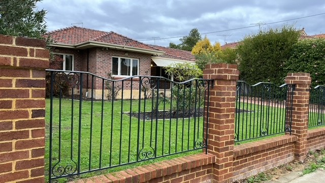 Brick house with garden and black iron fence.