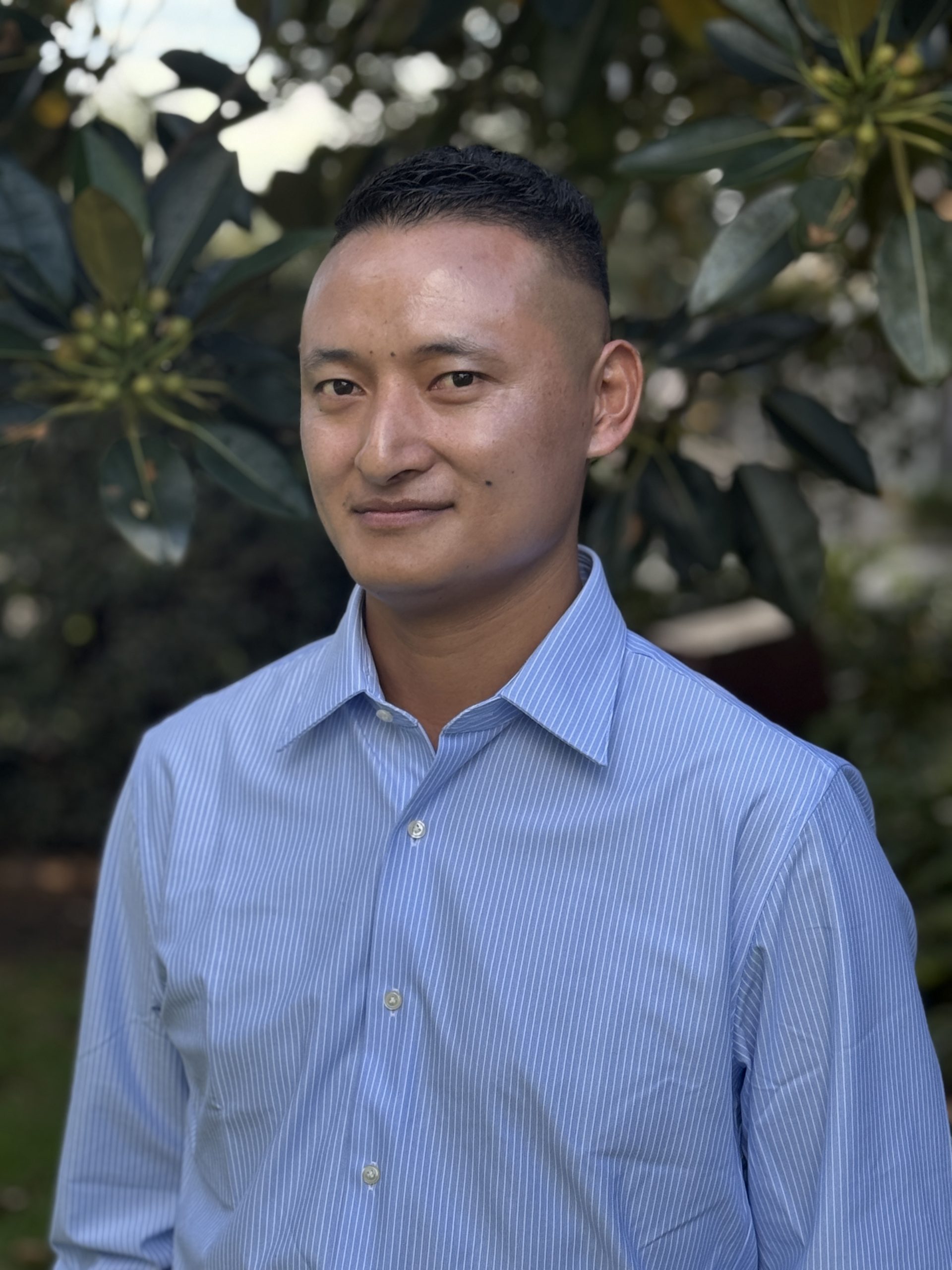 Person in blue shirt outdoors near tree.