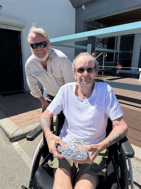 Smiling man with wheelchair holding foil-wrapped food.